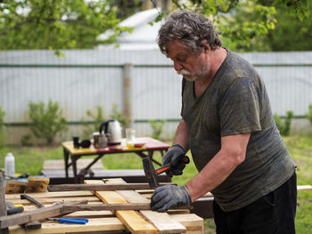 Mature caucasian man hammering a nail into a board in a garden