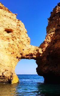 Rock formation by sea against clear blue sky