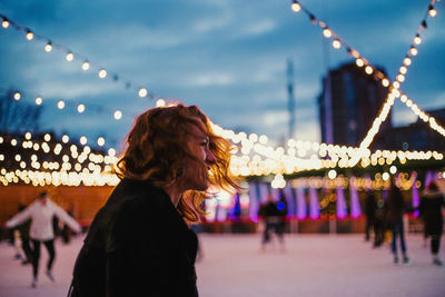 Woman with illuminated carousel against sky at night