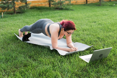 Rear view of woman using laptop while sitting on grassy field