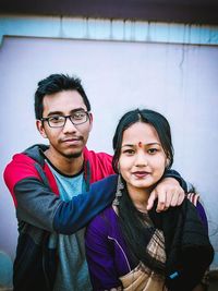 Portrait of smiling young couple standing against wall