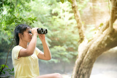 Young woman looking thorough binoculars in forest