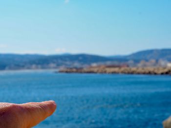 Cropped finger pointing at sea against sky