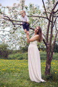 Pregnant girl with long hair and hold her son near the apple trees with white flowers