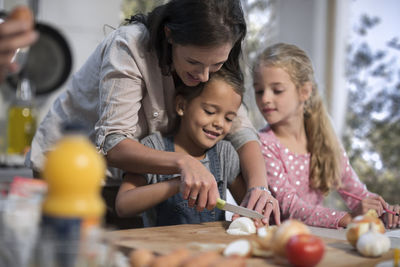 Mother helping daughters in kitchen