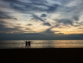 Silhouette people on beach against sky during sunset