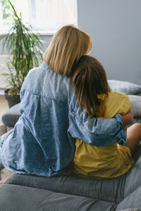 Rear view of mother and daughter sitting on sofa at home