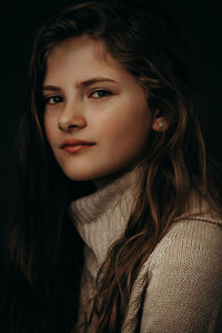 Close-up portrait of young woman against black background