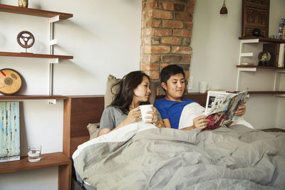 Husband and wife reading magazine while relaxing on bed at home