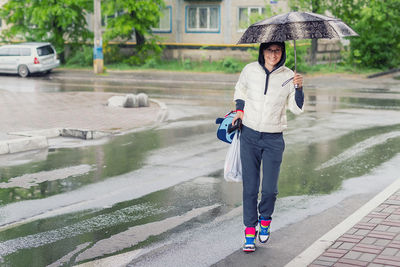 Full length of woman walking on wet street during monsoon