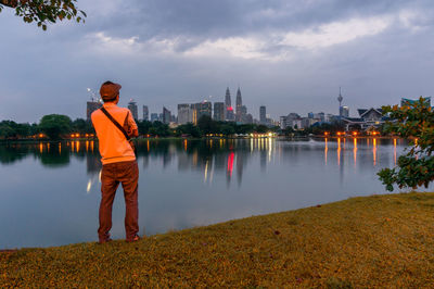 Man standing by river in city against sky