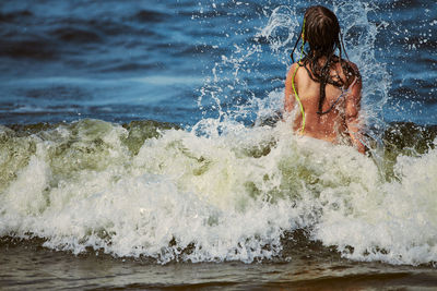 Rear view of shirtless man surfing in sea