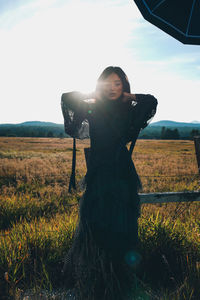 Woman with hand in hair standing on land against sky