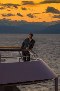 Man standing on boat in sea against sky during sunset