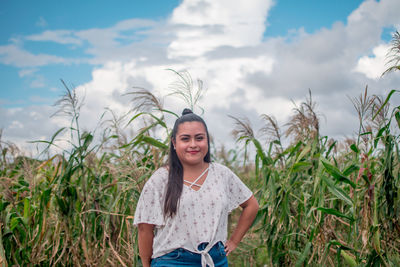 Portrait of smiling young woman standing on field against sky