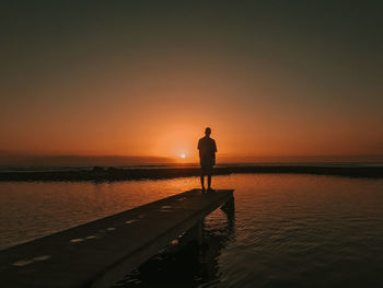 Silhouette man standing on beach against sky during sunset