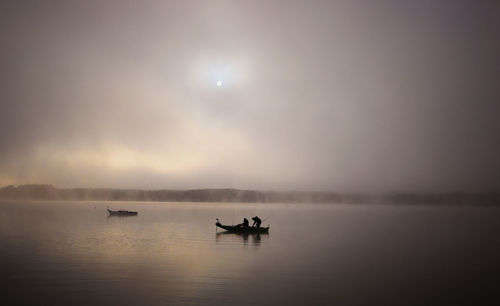 Silhouette people on boat in lake against sky during sunset