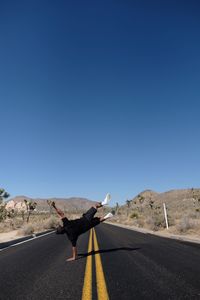 Full length of man doing stunt on road against clear sky