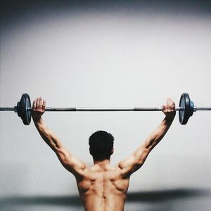 Rear view of muscular man lifted barbell against wall