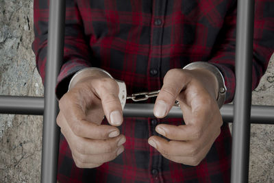 Midsection of man standing behind prison bars