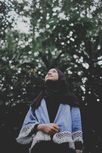 Thoughtful woman standing against trees