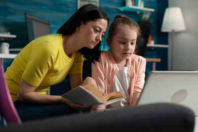 Young woman using phone while sitting on book