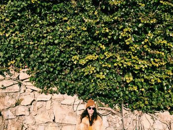 Woman standing against wall covered with plants