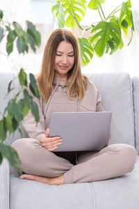 Smiling woman using laptop sitting on sofa at home