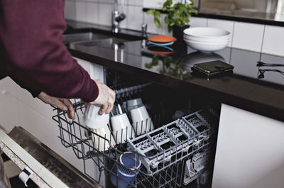 Cropped hands of senior man arranging cup in dishwasher at home