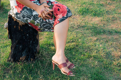 Low section of woman sitting on tree stump at field