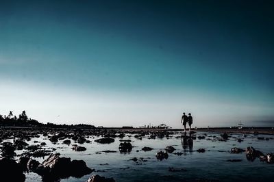 Silhouette people on beach against clear sky during sunset