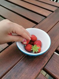 High angle view of hand holding strawberries in bowl on table