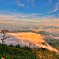 Scenic view of mountains covered with clouds against blue sky on sunny day