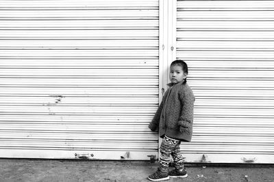 Portrait of boy standing against closed shutter