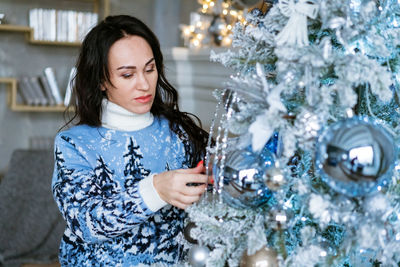 Beautiful brunette girl decorates an artificial christmas tree in blue winter