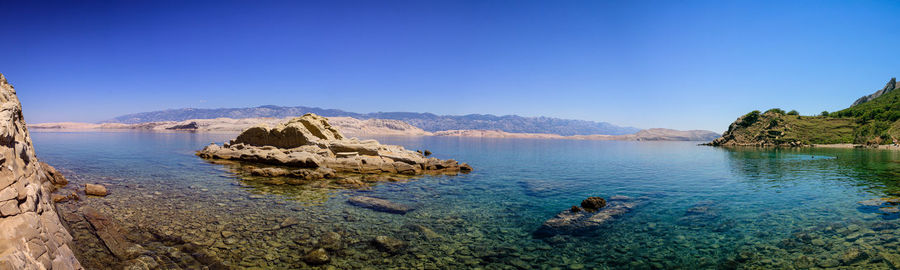 Panoramic view of sea and rocks against clear blue sky