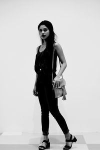 Full length portrait of young woman standing against white background