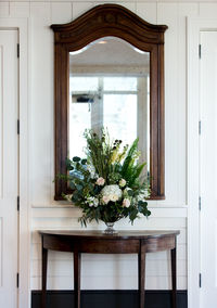 Flower vase on wooden table against mirror at home