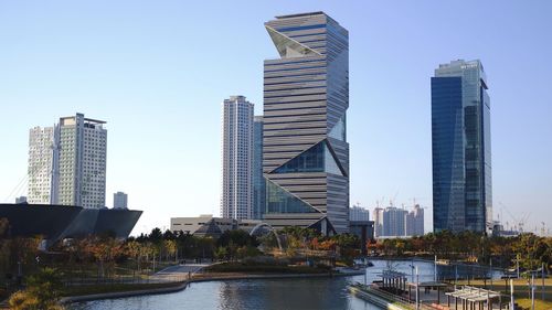 Modern buildings by river against sky in city