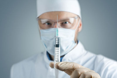 Portrait of doctor wearing mask holding syringe in hospital