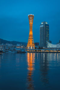 Illuminated buildings by sea against blue sky