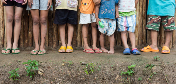 Low section of children standing against wooden fence