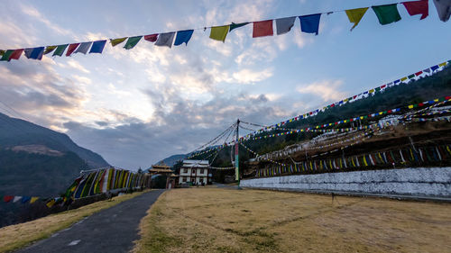 Multi colored flags hanging on bridge over mountain against sky