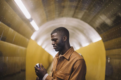 Young man opening water bottle while standing in tunnel