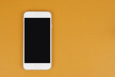 Close-up of smart phone against yellow wall