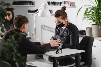 Male manicure. female nail service master doing manicure for adult man. man sitting in beauty salon