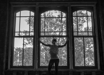 Rear view of woman standing by window in abandoned building
