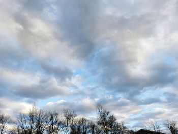 Low angle view of bare trees against cloudy sky