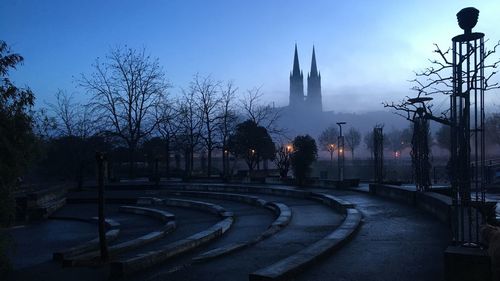 Bare trees and buildings against sky at dusk