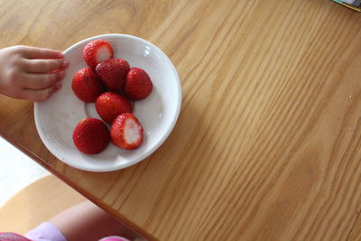 Midsection of person holding plate with strawberries on table at home